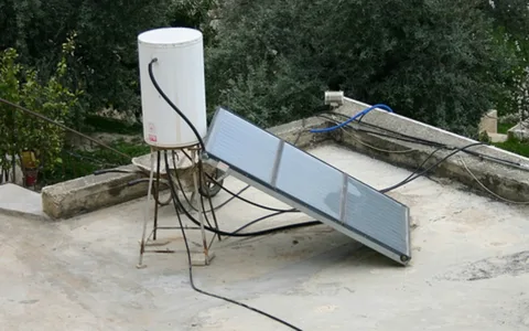  A homemade solar water heater made of black pipes and a wooden frame on a rooftop.